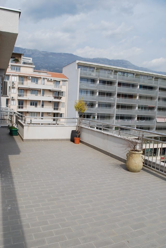 Prostrana terasa stana u Budvi, Crna Gora, s pogledom na planine i gradsku arhitekturu, pločice na podu i dekor.