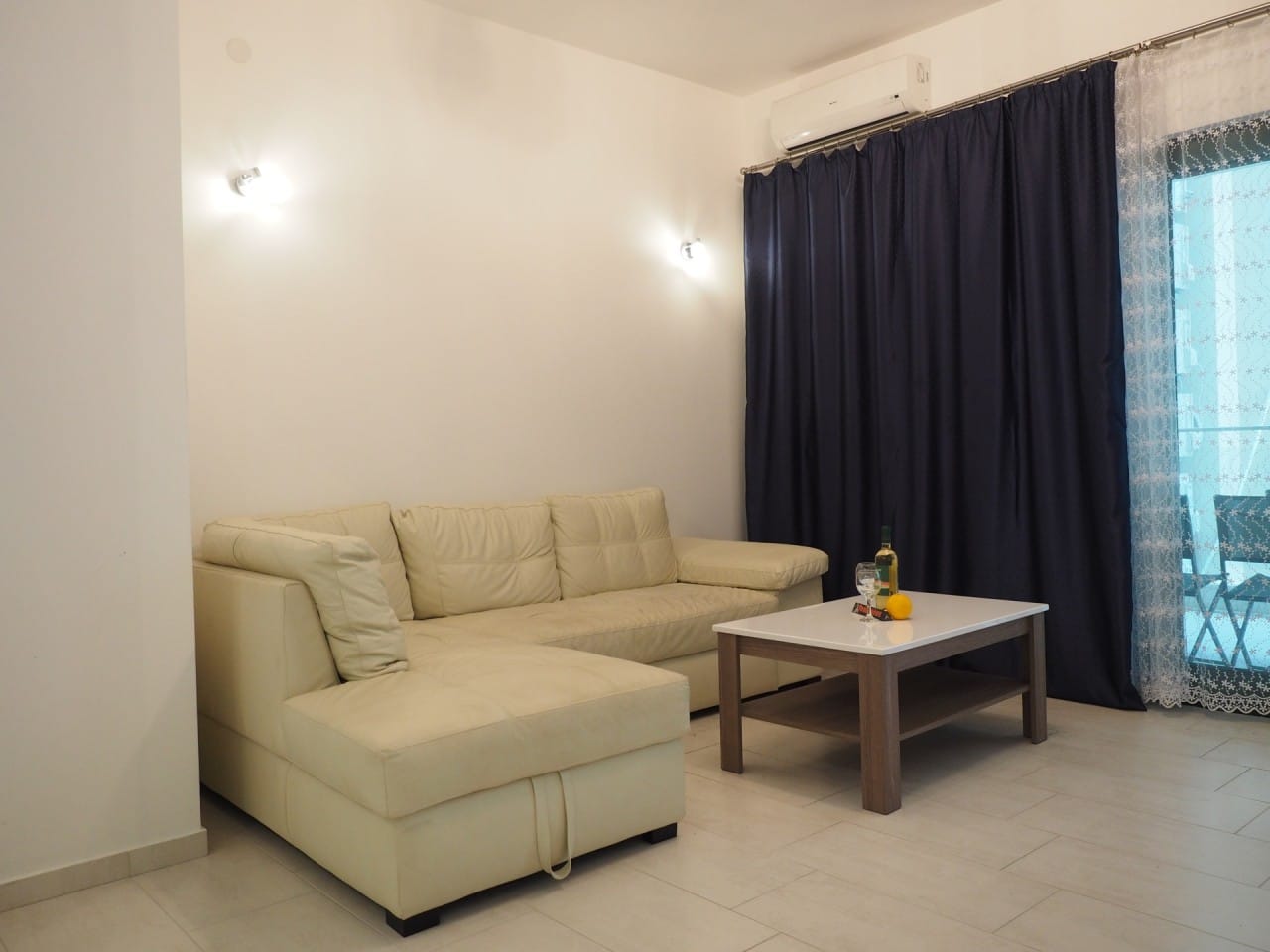 Dnevna soba sa belom kožnom sofom i klub stolom u stanu u Pržnu, Crna Gora, izlaz na balkon.