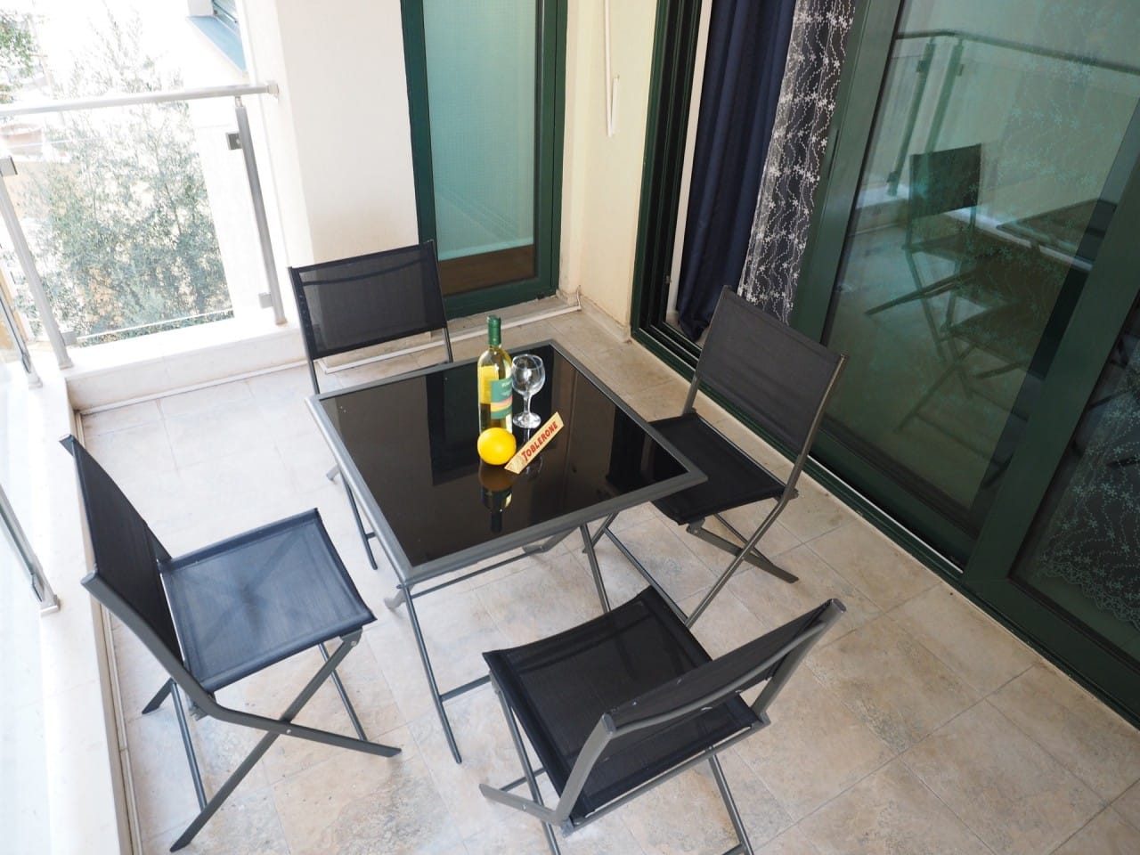 Udoban balkon sa nameštajem i staklenim stolom u stanu u Pržnu, Crna Gora, pogled na zelenilo i terasu.