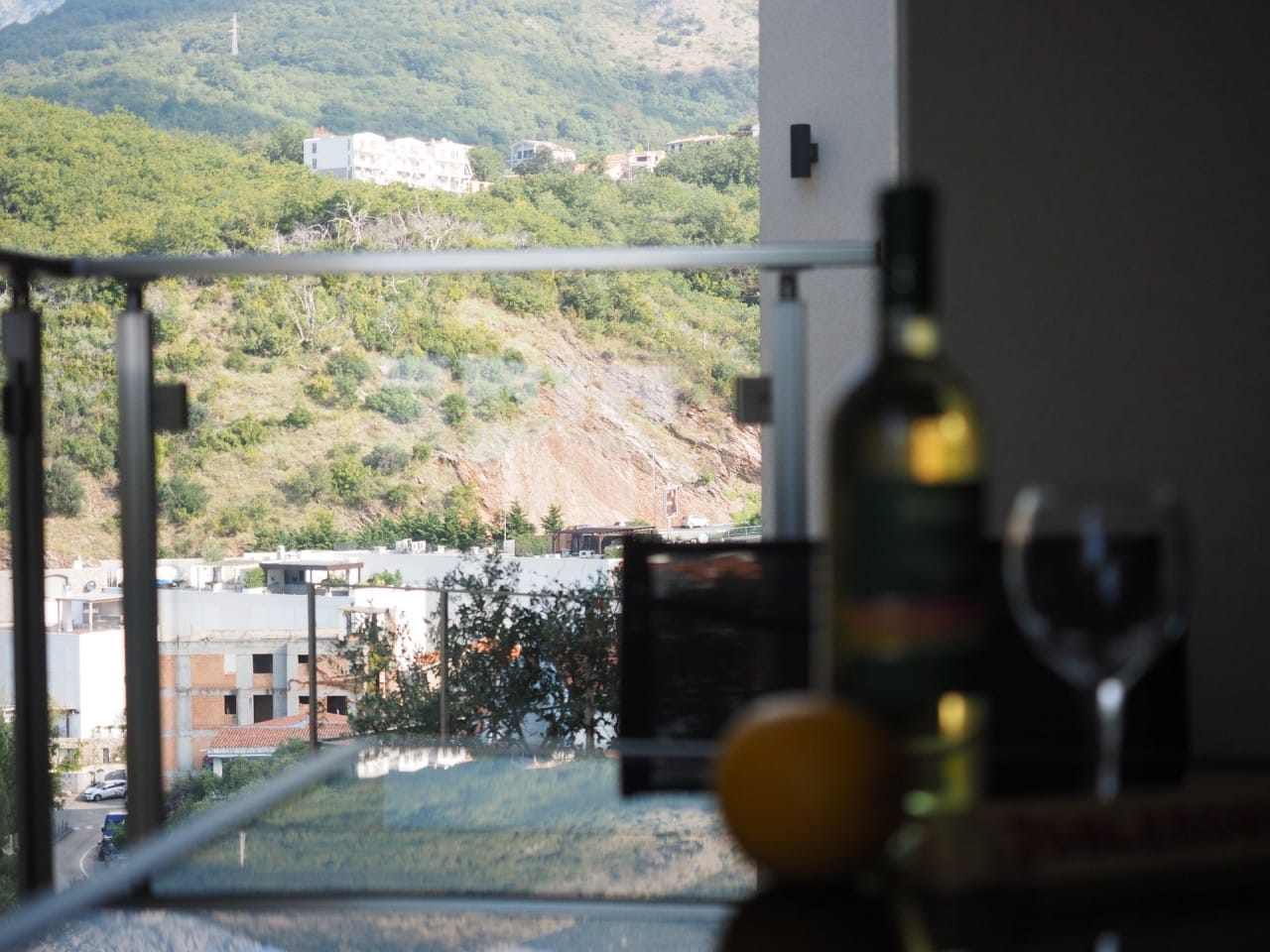 Pogled sa balkona stana u Pržnu, Crna Gora: stakleni sto sa vinom u pozadini planinskog pejzaža i moderne gradnje.