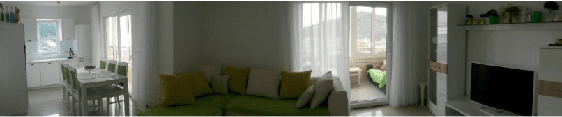 Wohnzimmer mit Küche in einer Wohnung in Budva, Montenegro: helle Möbel, Ecksofa und Zugang zum Balkon mit Bergblick.