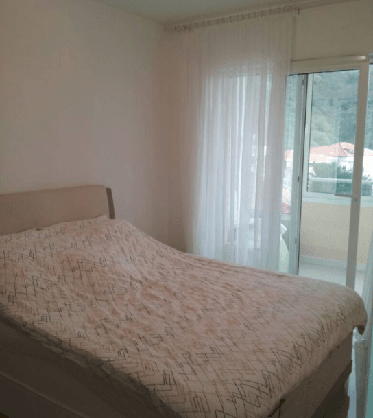 Schlafzimmer in einer Wohnung in Budva, Montenegro: Doppelbett, helle Wände und Zugang zum Balkon mit Bergblick.