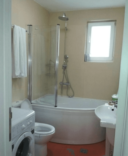 Badezimmer in einer Wohnung in Budva, Montenegro: Eckbadewanne mit Duschabtrennung, Waschbecken und Waschmaschine.