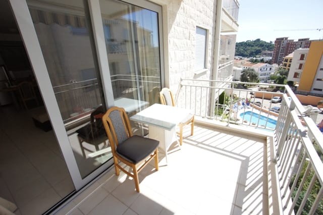 Balkon s nameštajem i pogledom na bazen u stanu u Petrovcu, Crna Gora: svetla terasa s panoramskim ostakljenjem.