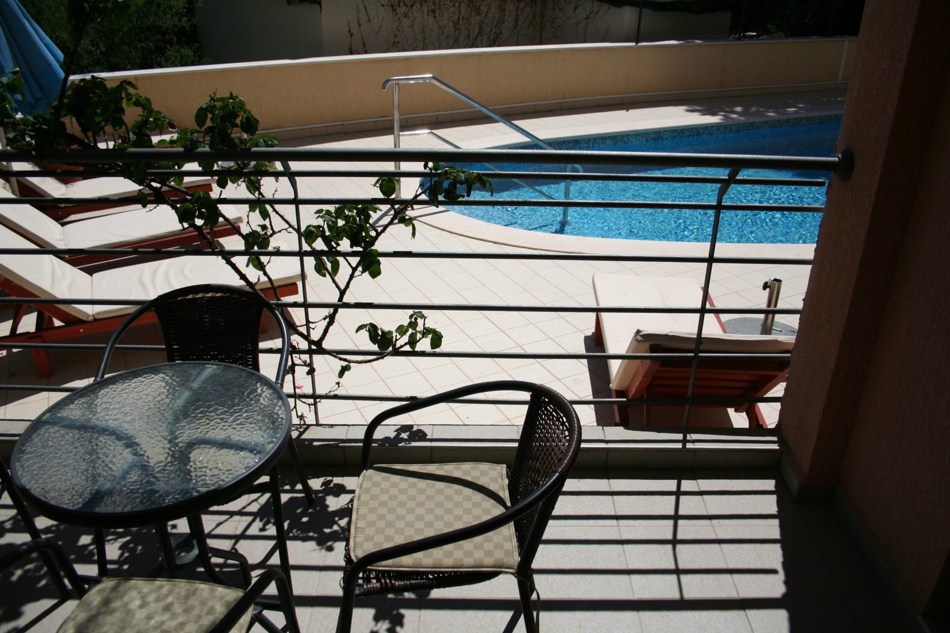 Balkon sa nameštajem i pogledom na otvoreni bazen u stanu u Bečićima, Crna Gora. Udobna zona za odmor pored vode.