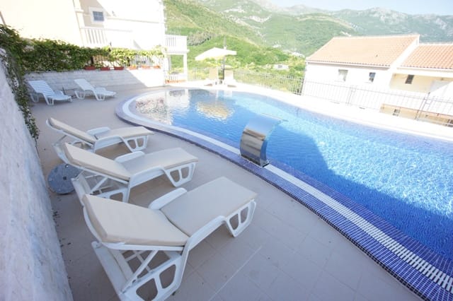 Otvoreni bazen sa ležaljkama na terasi stambenog kompleksa u Bečićima, Crna Gora, s pogledom na zelene planine.