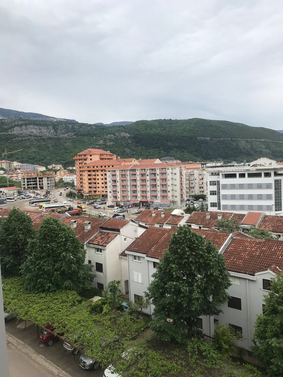 Panoramski pogled iz prozora stana u Budvi, Crna Gora: gradska izgradnja, krovovi od crepova i zelene planine u pozadini.