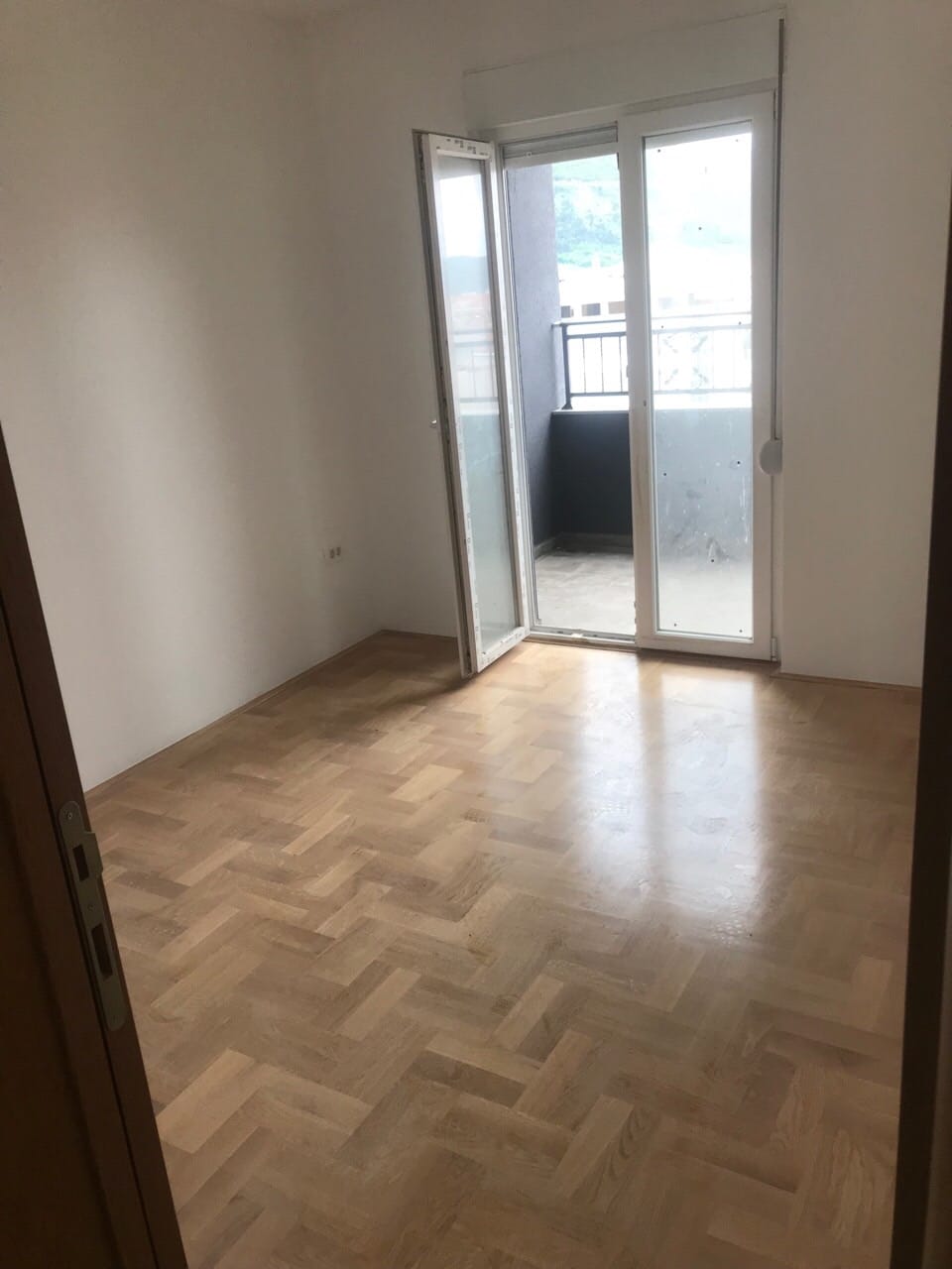 Svetla spavaća soba sa parketom i izlazom na balkon u stanu, Budva, Crna Gora.