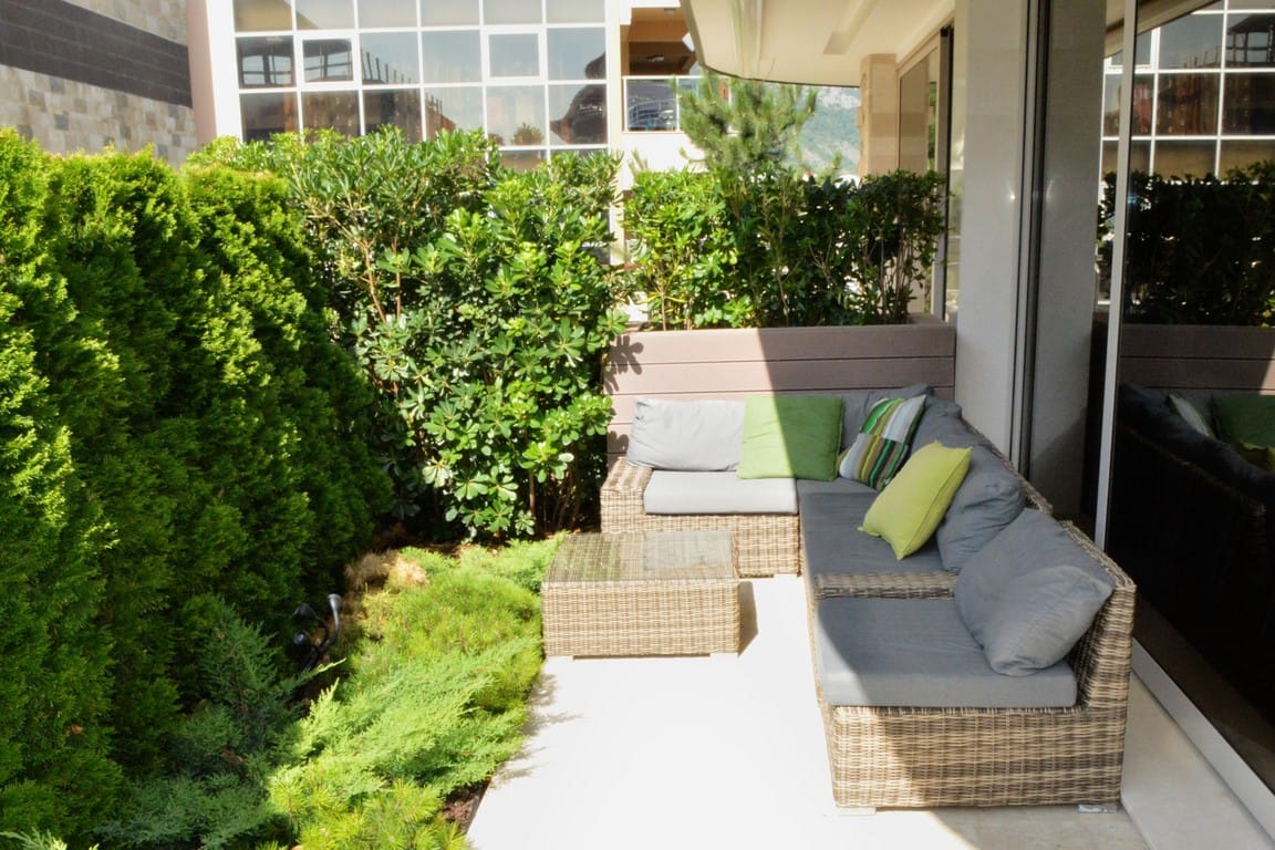 Ugodna terasa s pletenim nameštajem i živom ogradom u stanu u Budvi, Crna Gora. Pogled na uređeni balkon.