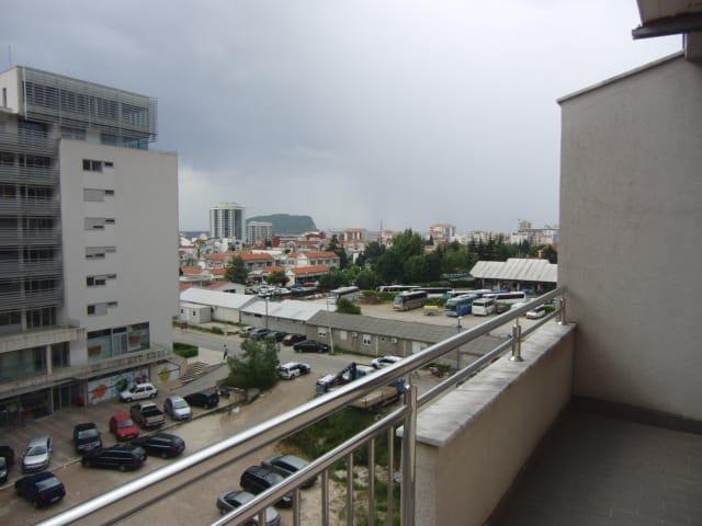Pogled sa balkona stana u Budvi, Crna Gora: panorama grada, parking i stambene zgrade na pešačkoj udaljenosti.
