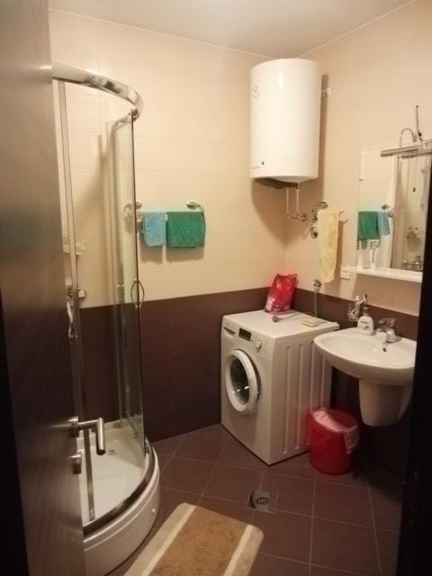 Kupatilo u stanu u Budvi, Crna Gora: tuš kabina, veš mašina, bojler i lavabo sa ogledalom.