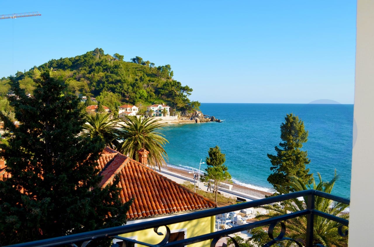 Pogled s balkona na more, plažu i zelene brežuljke u gradu Petrovac, Crna Gora. Panorama obale sa terase stana.