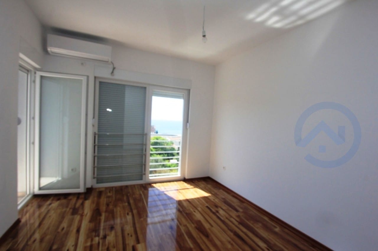 Helles Wohnzimmer mit Parkett und Zugang zum Balkon mit Meerblick in einer Wohnung, Stadt Petrovac, Montenegro.