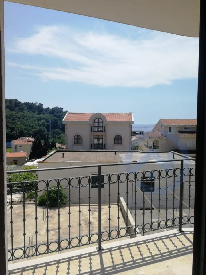 Vue depuis le balcon d’un appartement à Petrovac, Monténégro : garde-corps en fer forgé, panorama de la ville, collines et horizon marin.