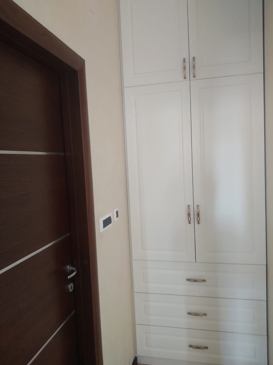 Ugradni beli ormar sa fiokama u spavaćoj sobi stana u Budvi, Crna Gora, pored tamnih unutrašnjih vrata.