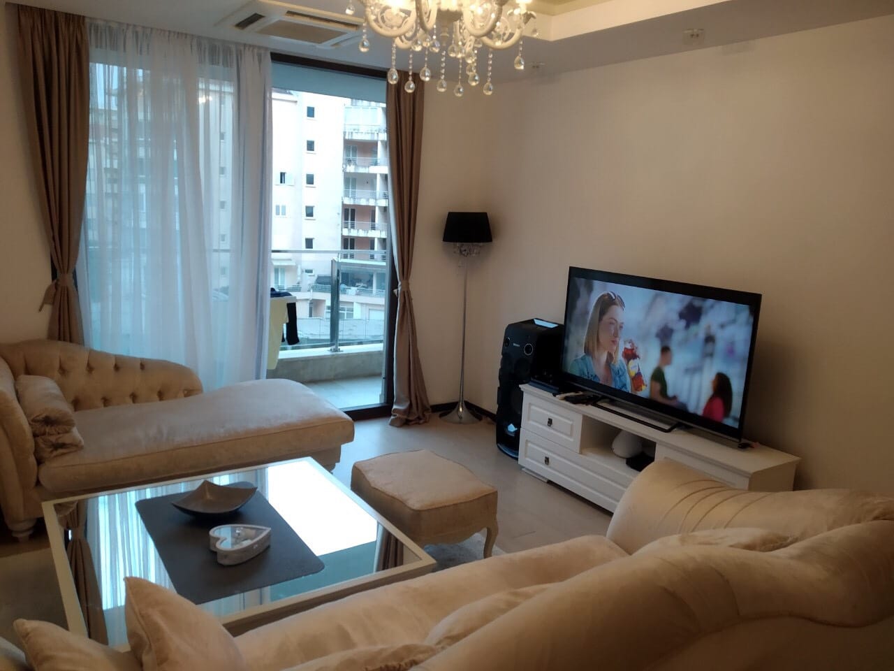 Udoban dnevni boravak u stanu u Budvi, Crna Gora: bež meblirana garnitura, stakleni sto i izlaz na balkon.