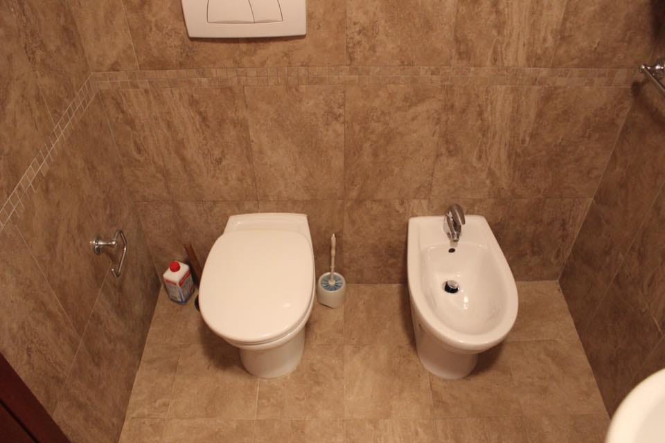 Kupatilo sa toaletom i bideom u stanu u Rafailovićima, Crna Gora, zidovi obloženi bež pločicama u imitaciji kamena.