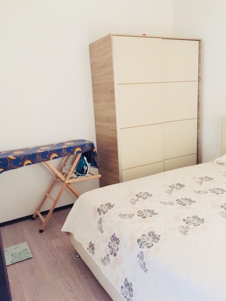 Spavaća soba u stanu u Budvi, Crna Gora: bračni krevet, svetli ugradni ormar i daska za peglanje u enterijeru.