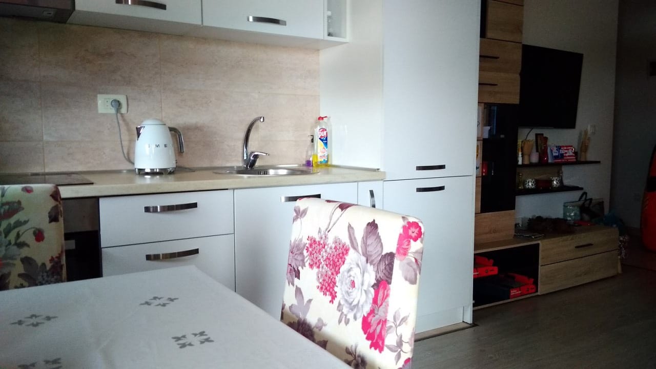 Savremena kuhinja u stanu u Budvi, Crna Gora: beli frontovi, trpezarijski deo sa stolicama s cvetnim dezenom i TV zona.