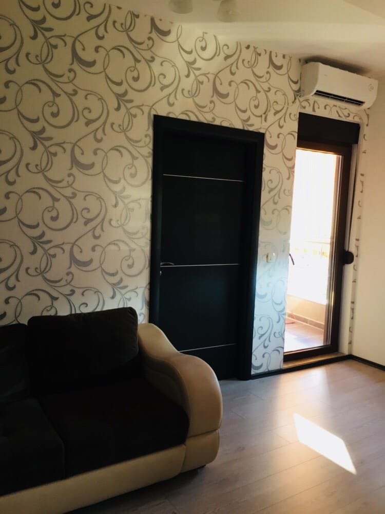 Dnevna soba u stanu u Budvi, Crna Gora: svetle tapete s uzorkom, tamna unutrašnja vrata i izlaz na balkon.