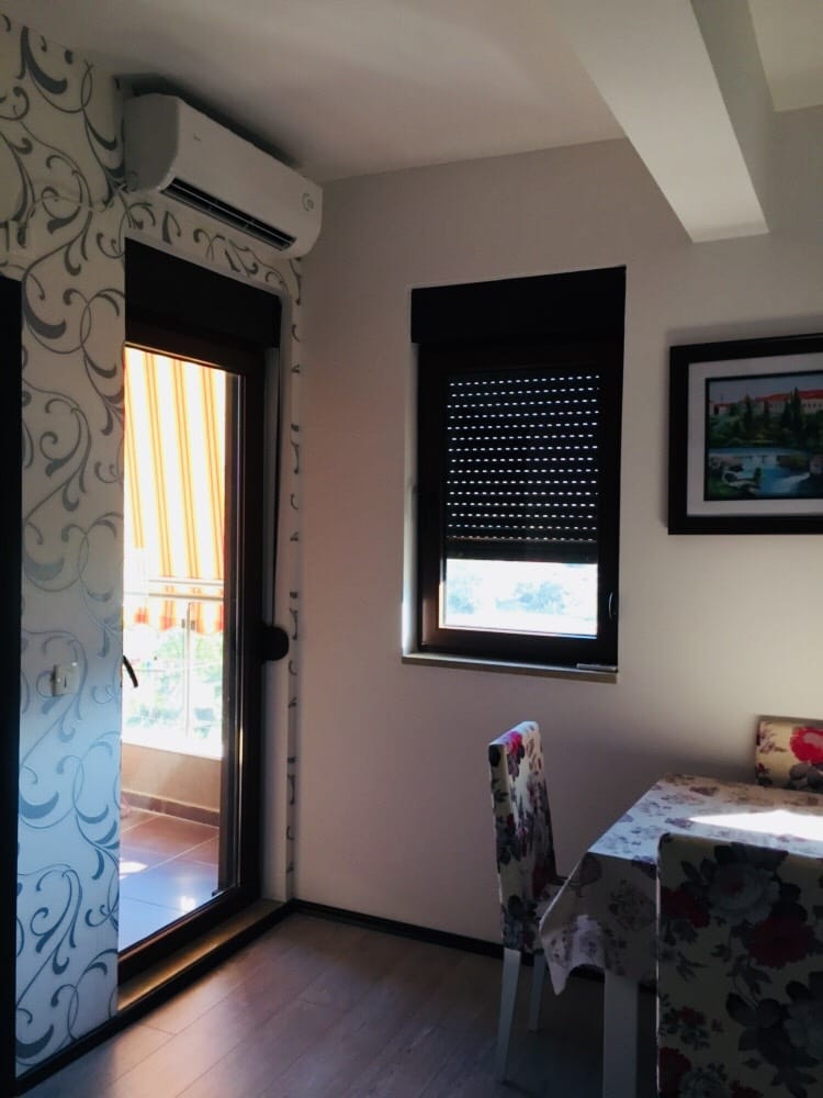 Dnevna soba sa izlazom na balkon u stanu u Budvi, Crna Gora: svetao enterijer, klima-uređaj i trpezarijski deo.