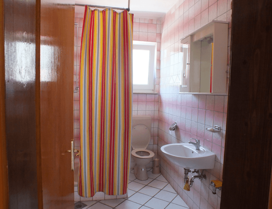 Bathroom in a house in Bar, Montenegro: light tile, a shower area with a bright curtain, a sink, and a toilet.