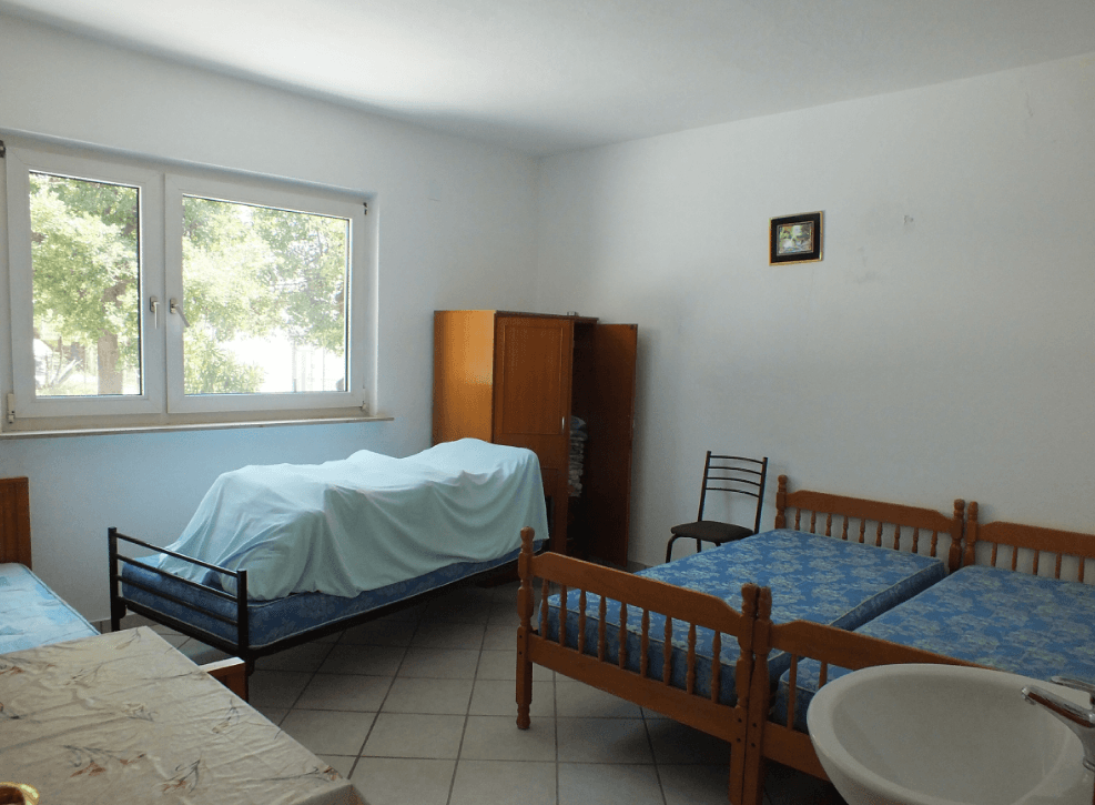 Bright bedroom with three beds and a sink in a house for sale in Bar, Montenegro. View of a green garden.