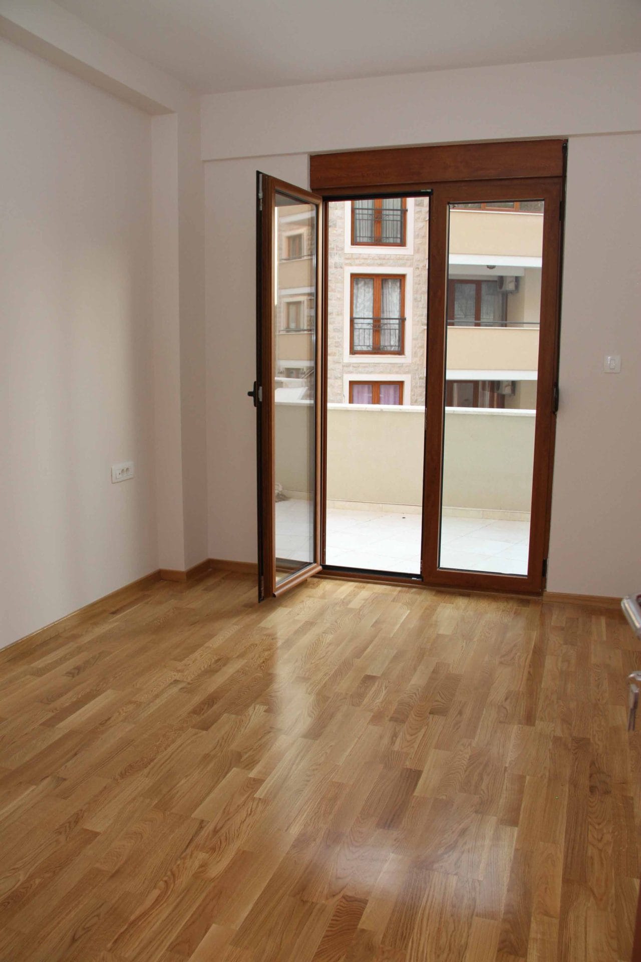 Bright living room with parquet flooring and access to the balcony in an apartment in Petrovac, Montenegro. View of neighboring buildings.