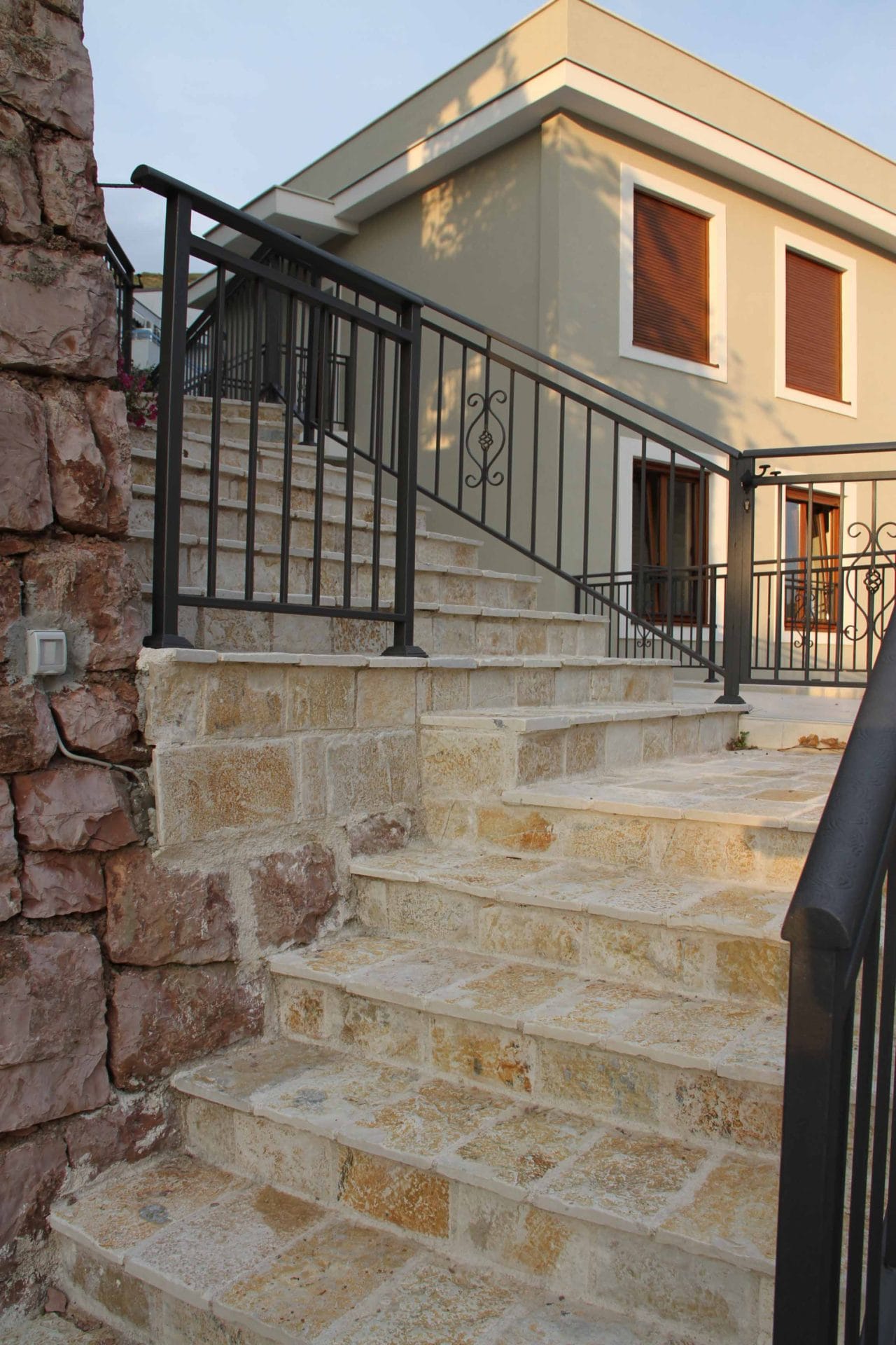 Stone staircase with wrought-iron railings at the entrance to a house in Petrovac, Montenegro. Facade finished with natural stone.