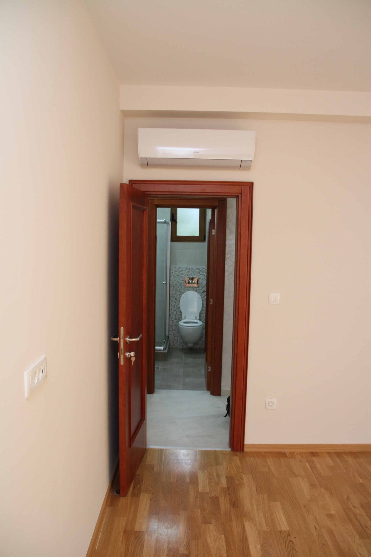 View from the bedroom to the bathroom in an apartment in Petrovac, Montenegro: light finishes, air conditioning, and wooden doors.