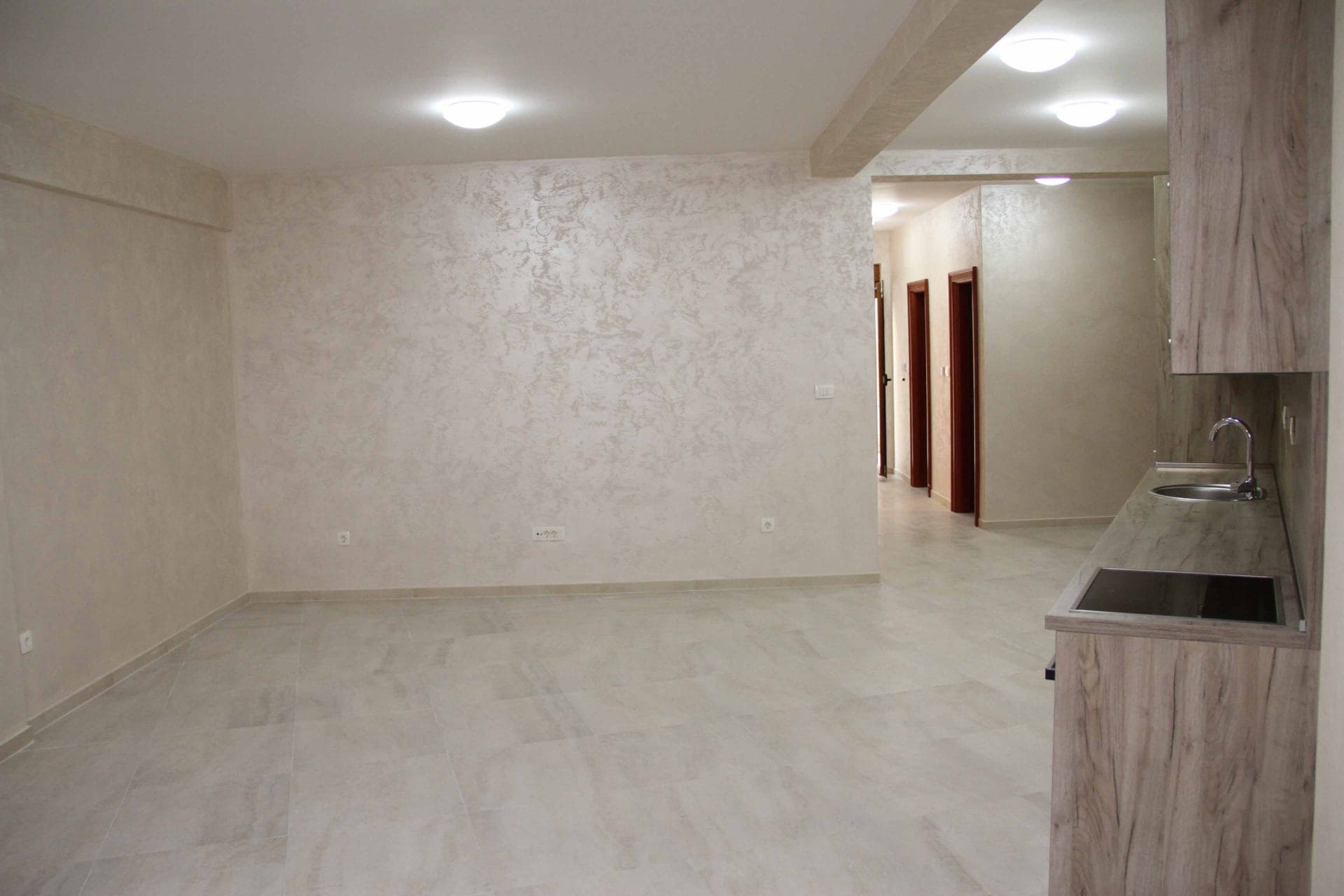 Bright living room with kitchen in an apartment in Petrovac, Montenegro: decorative plaster, tiled floor, and kitchen cabinets.