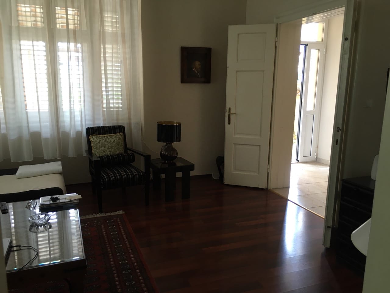 Karadağ, Herceg Novi’deki evde oturma odası: koyu parke, çizgili koltuk, sehpa ve terasa çıkış.