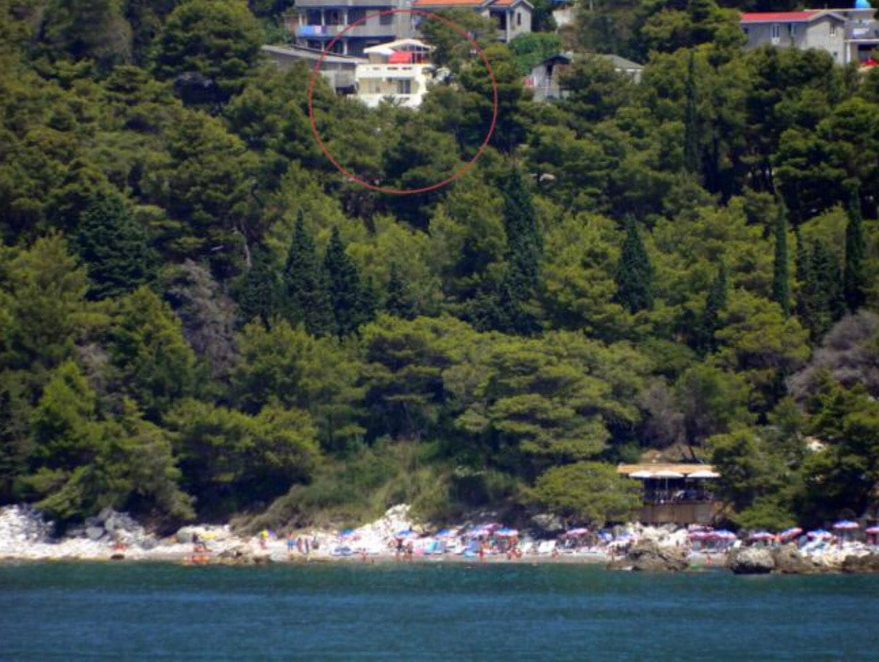 White house surrounded by pine forest by the sea in Bar, Montenegro, with an elevated view of the coastline and beach.
