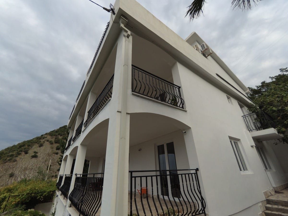 Karadağ, Bečići’de teraslı ve ferforje korkuluklu beyaz üç katlı villa. Evin cephesi ve dağ manzarası.