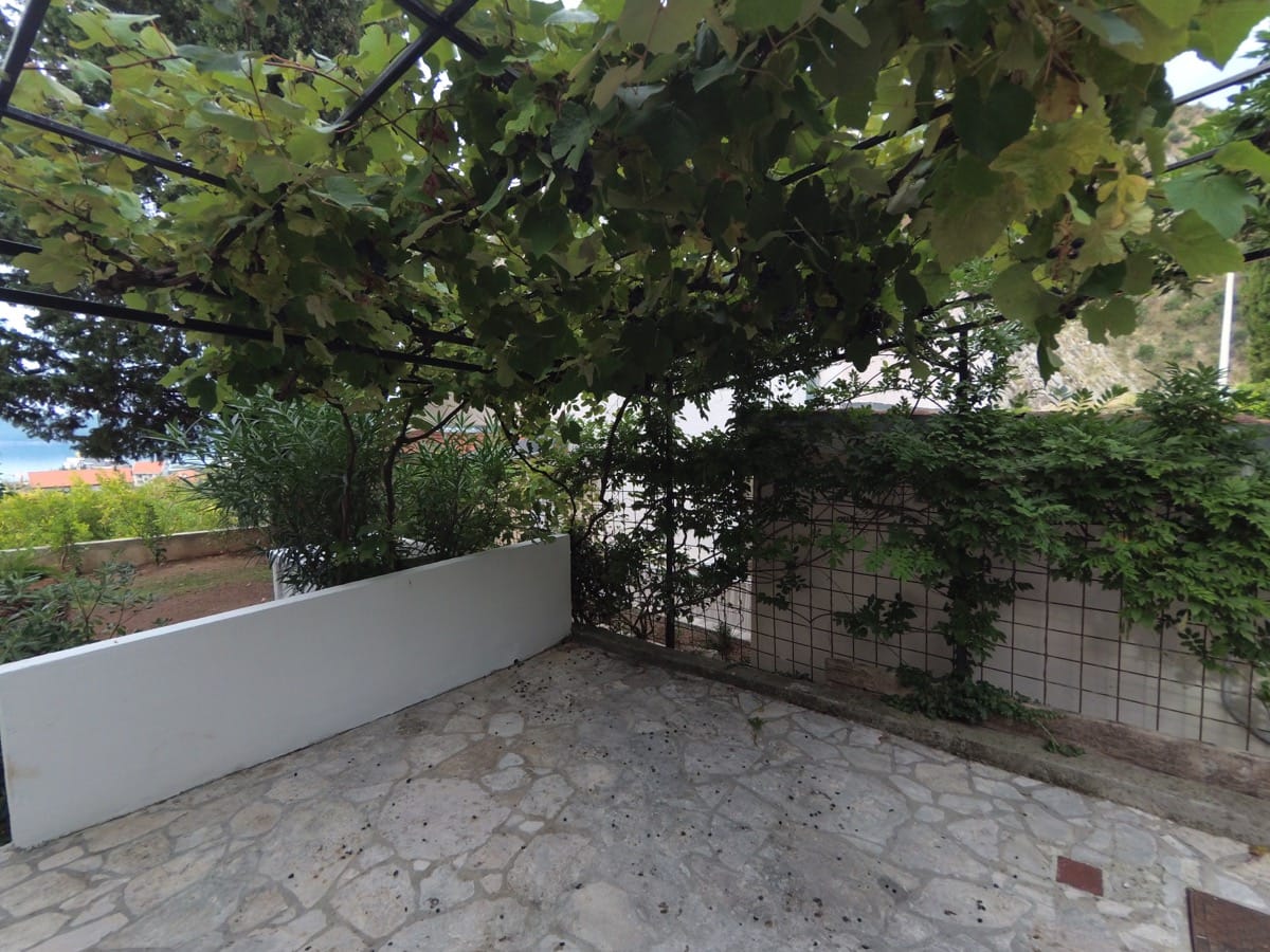 Becici, Karadağ’daki villada üzüm pergolalı ve taş zeminli уютная teras. Bahçe ve dağ manzarası.