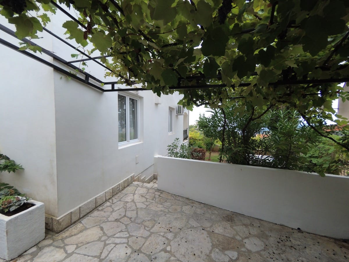 Karadağ, Bečići’de taş kaplamalı, üzüm asmalı pergolalı ve yeşil bahçeli уютная villa terası.