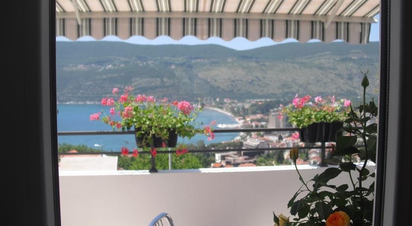 Karadağ, Herceg Novi’deki evin balkonundan görünüm: deniz, dağlar ve şehrin panoraması, saksılarda çiçekler, güneşten koruyucu tente.