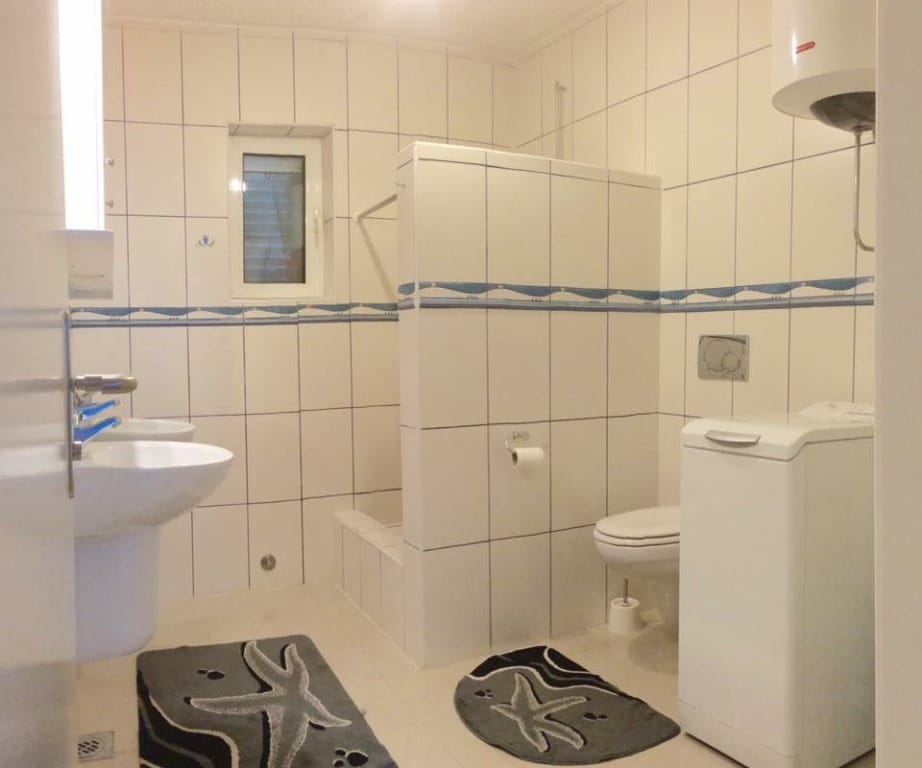 Svetlo kupatilo sa tuš kabinom i veš mašinom u mini-hotelu, Meline, Bokokotorski zaliv, Crna Gora.