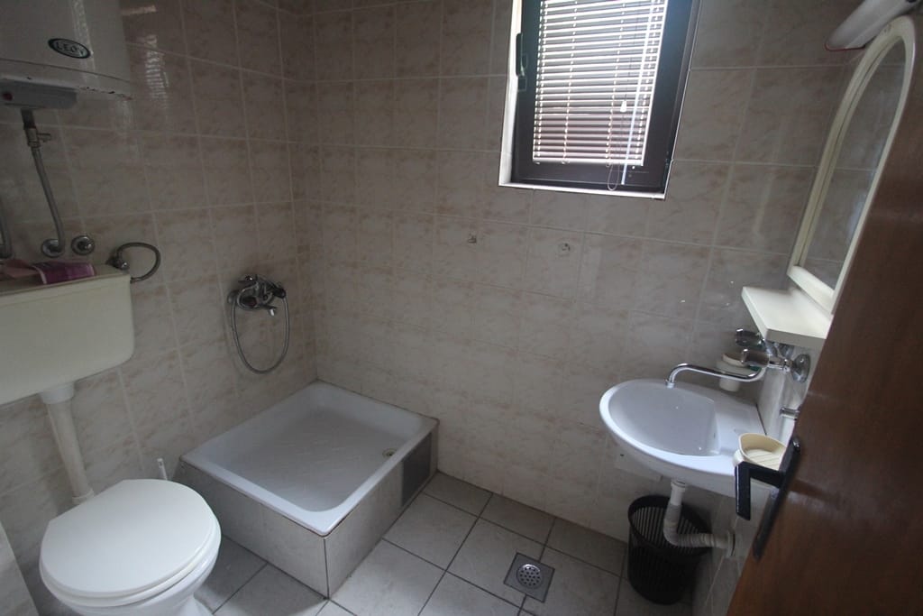 Kupatilo u mini-hotelu u Baošićima, Crna Gora: svetle pločice, tuš-kada, lavabo i bojler.