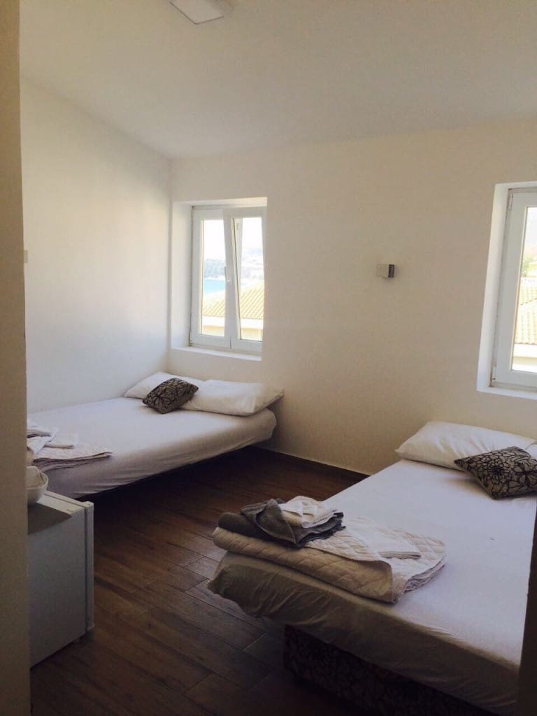 Spavaća soba u mini-hotelu Rafailovići, Crna Gora: dva kreveta, svetao enterijer, drveni pod i pogled na more kroz prozor.