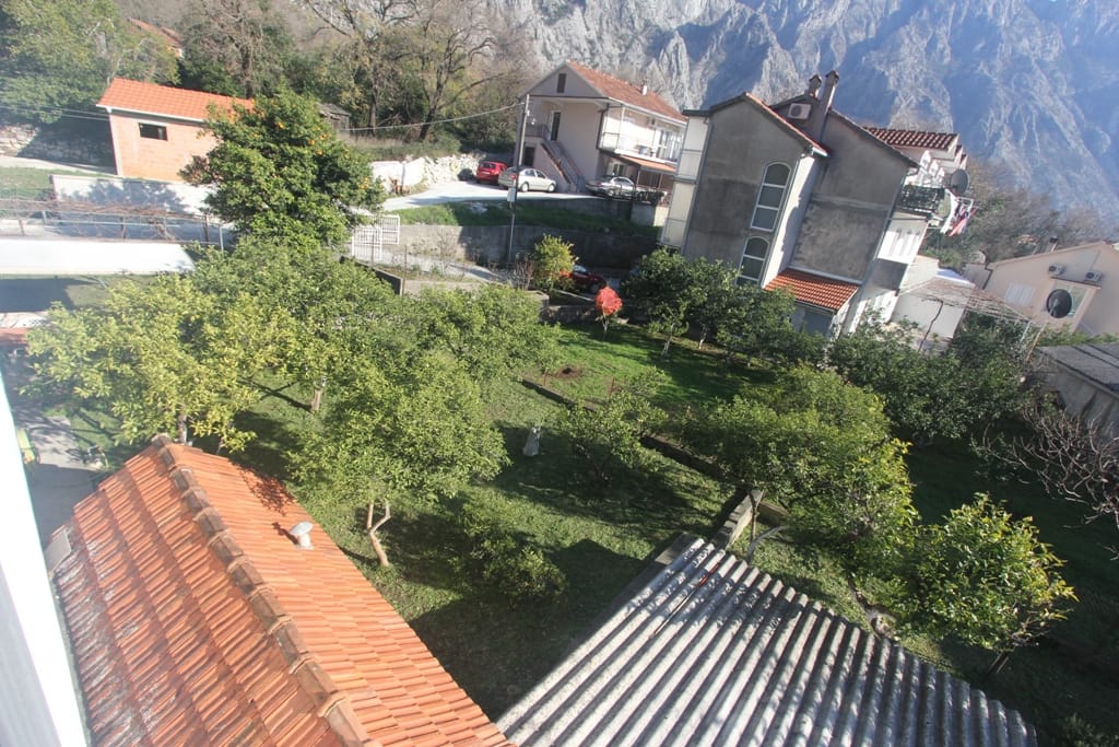 Blick auf den grünen Garten und die Berge von der Terrasse des Hauses in Orahovac, Montenegro: Ziegeldächer und privates Grundstück mit Bäumen.