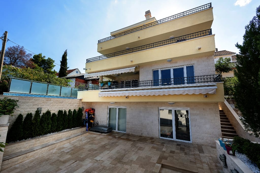 Karadağ, Krašići’de üç katlı villa: taş cepheli, ferforje korkuluklu teraslar ve уютный iç avlu.