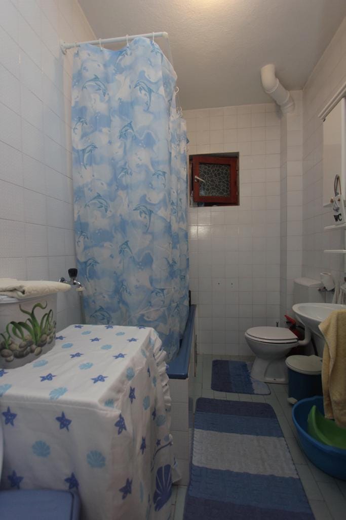 Badezimmer im Haus, Herceg Novi, Montenegro: weiße Fliesen, blaue Duschvorhang mit Delfinen, Sanitäranlagen und Fenster.