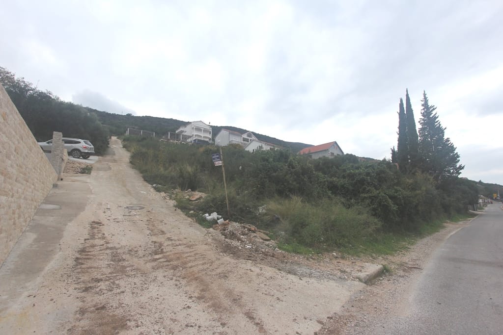 Karadağ, Krašići'de inşaata uygun arsa: giriş yolu, engebeli arazi ve çevredeki evlerin görünümü.
