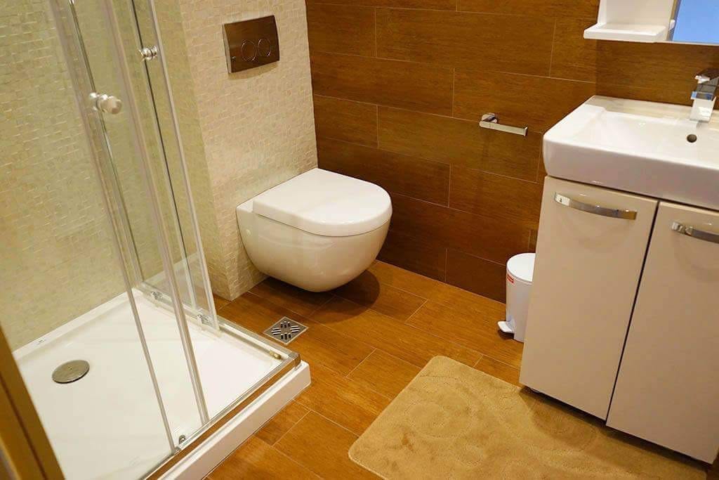 Modernes Badezimmer mit Duschkabine in einer Wohnung in Budva, Montenegro: Holzoptik-Fliesen und Sanitäranlagen.