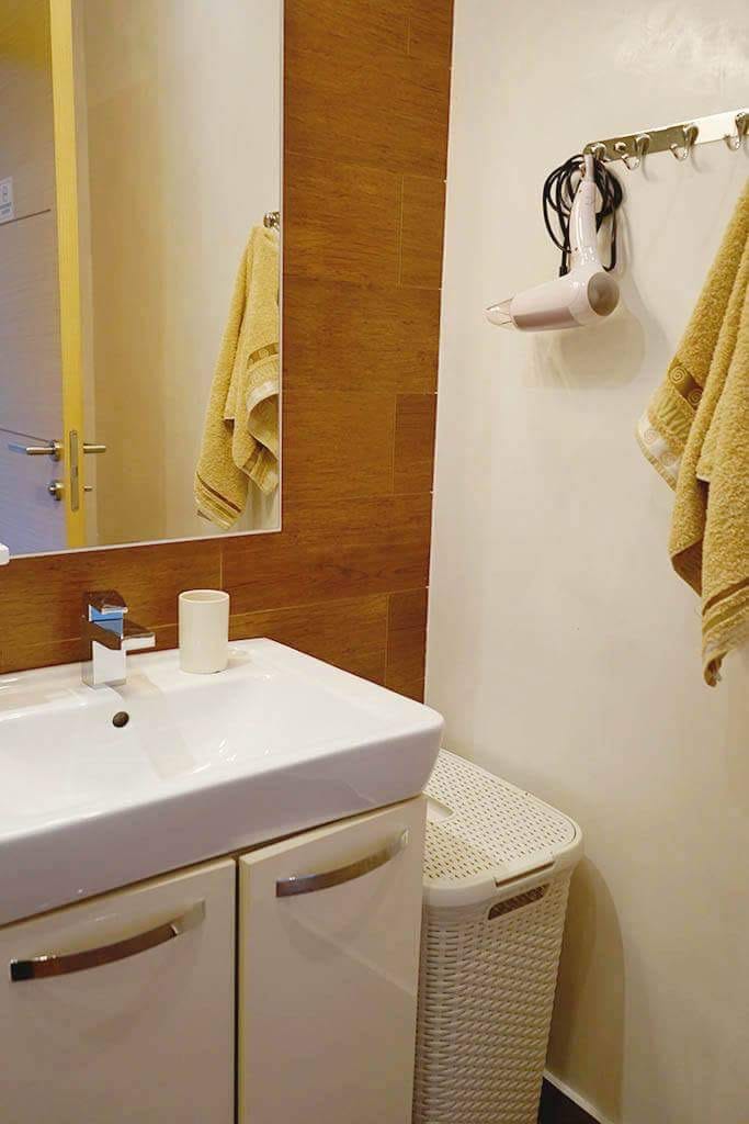 Modernes Badezimmer in einer Wohnung in Budva, Montenegro: weiße Waschtischanlage mit Waschbecken, Spiegel und Holzoptik-Verkleidung.