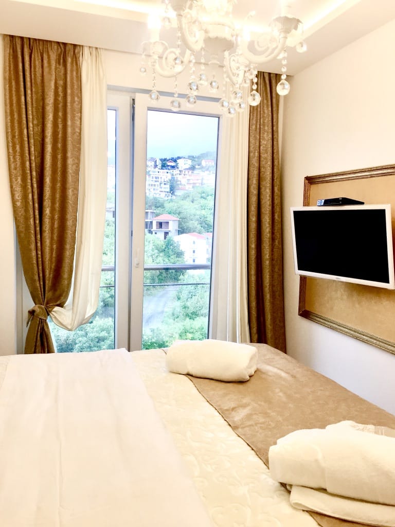 Udobna spavaća soba u stanu u Bečićima, Crna Gora: bračni krevet, TV, kristalni luster i pogled na planine.