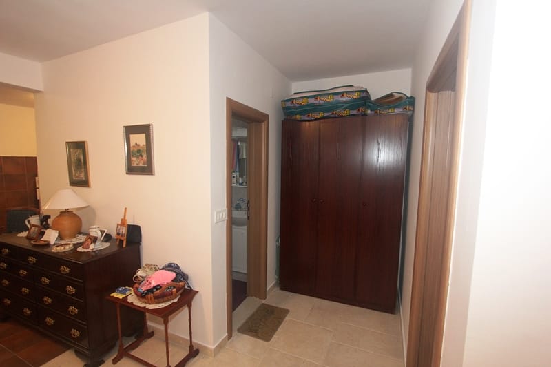 Enterijer dnevne sobe sa tamnim drvenim komodom i ormarom u stanu, Pržno, Crna Gora. Svetla obrada i pod od pločica.