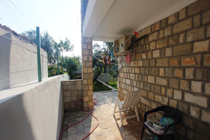 Ugodna terasa sa kamenim oblogama i baštenskim nameštajem u stanu u Pržnu, Crna Gora. Pogled na zelenu baštu i balkon.