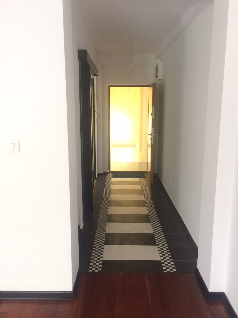 Svetao hodnik u stanu u Petrovcu, Crna Gora: pod sa crno-belom pločicom, beli zidovi i ulazna vrata.
